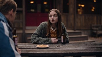Movie still from “The End of the F***ing World” (2017), directed by Jonathan Entwistle – A woman sitting at a wooden table with a bottle of beer; Medium shot, Over the shoulder angle