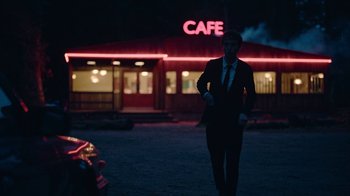 Movie still from “The End of the F***ing World” (2017), directed by Jonathan Entwistle – A man in a suit and tie walking in front of a cafe at night; Wide shot, Over the shoulder angle