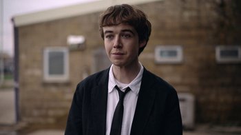 Movie still from “The End of the F***ing World” (2017), directed by Jonathan Entwistle – A man in a suit and tie standing in front of a brick wall; Close Up shot, Over the shoulder angle