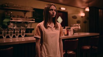 Movie still from “The End of the F***ing World” (2017), directed by Jonathan Entwistle – A woman standing in front of a counter; Medium shot, Over the shoulder angle