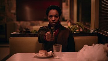 Movie still from “The End of the F***ing World” (2017), directed by Jonathan Entwistle – A person sitting at a dinner table holding a gun; Medium shot, Low angle
