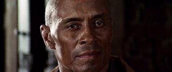 Movie still from “Once Upon a Time in the West” (1968), directed by Sergio Leone – An older man with a shaved head and a goatee looking at the camera; Close Up shot, Low angle