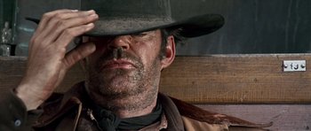 Movie still from “Once Upon a Time in the West” (1968), directed by Sergio Leone – A man in a cowboy hat is sitting on a bench; Close Up shot, Low angle