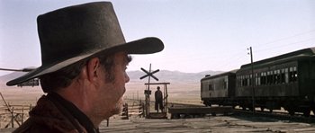 Movie still from “Once Upon a Time in the West” (1968), directed by Sergio Leone – A man wearing a cowboy hat standing in front of a train; Wide shot, Low angle