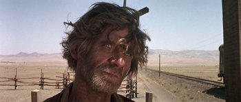 Movie still from “Once Upon a Time in the West” (1968), directed by Sergio Leone – A man with long hair and a beard standing next to a wooden cross; Close Up shot, Low angle