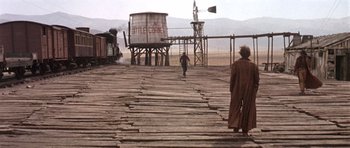 Movie still from “Once Upon a Time in the West” (1968), directed by Sergio Leone – A man walking across a wooden walkway next to a water tower; Wide shot, Low angle