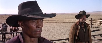Movie still from “Once Upon a Time in the West” (1968), directed by Sergio Leone – A man wearing a cowboy hat standing next to a field; Close Up shot, Over the shoulder angle