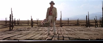 Movie still from “Once Upon a Time in the West” (1968), directed by Sergio Leone – A man standing on top of a brick road holding a suitcase; Wide shot, Low angle