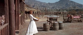 Movie still from “Once Upon a Time in the West” (1968), directed by Sergio Leone – A woman in a white dress standing next to barrels; Wide shot, Low angle