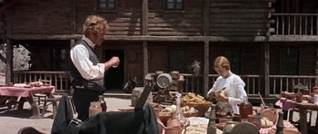 Movie still from “Once Upon a Time in the West” (1968), directed by Sergio Leone – A man standing next to a woman in front of a table; Medium shot, Low angle