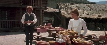 Movie still from “Once Upon a Time in the West” (1968), directed by Sergio Leone – A woman standing next to a table filled with food; Medium shot, Over the shoulder angle