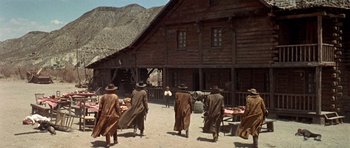 Movie still from “Once Upon a Time in the West” (1968), directed by Sergio Leone – A group of men in long coats and hats walking in front of a building; Wide shot, Low angle