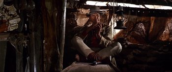 Movie still from “Once Upon a Time in the West” (1968), directed by Sergio Leone – A man sitting on the ground with a hat on his head; Wide shot, Low angle