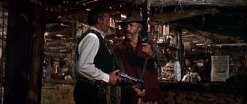 Movie still from “Once Upon a Time in the West” (1968), directed by Sergio Leone – A man holding a gun while standing next to another man holding a gun; Medium shot, Low angle
