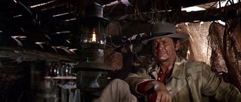 Movie still from “Once Upon a Time in the West” (1968), directed by Sergio Leone – A man sitting next to an oil lamp in a room; Medium shot, Low angle