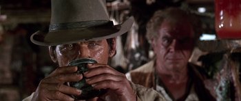 Movie still from “Once Upon a Time in the West” (1968), directed by Sergio Leone – A man in a cowboy hat drinking from a cup; Close Up shot, Over the shoulder angle
