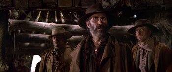 Movie still from “Once Upon a Time in the West” (1968), directed by Sergio Leone – A man with a beard wearing a hat and a brown jacket; Medium shot, Low angle