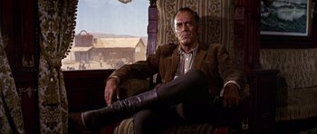 Movie still from “Once Upon a Time in the West” (1968), directed by Sergio Leone – An older man sitting in a chair with his legs crossed; Medium shot, Low angle
