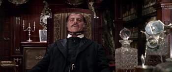 Movie still from “Once Upon a Time in the West” (1968), directed by Sergio Leone – A man in a suit and tie standing next to a chair; Medium shot, Low angle