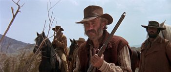 Movie still from “Once Upon a Time in the West” (1968), directed by Sergio Leone – A man holding a gun while standing next to a horse; Medium shot, Low angle