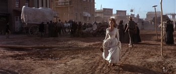 Movie still from “Once Upon a Time in the West” (1968), directed by Sergio Leone – A woman in a white dress walking in a dirt field; Wide shot, Low angle