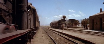 Movie still from “Once Upon a Time in the West” (1968), directed by Sergio Leone – A man walking across a train track next to two trains; Extreme Wide shot, Low angle