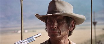 Movie still from “Once Upon a Time in the West” (1968), directed by Sergio Leone – A person wearing a hat and holding a gun; Close Up shot, Low angle