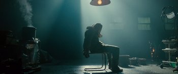 Movie still from “The Expendables 2” (2012), directed by Simon West – A person sitting on a chair in a room with lights; Wide shot, Low angle