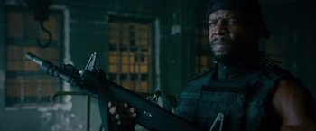Movie still from “The Expendables 2” (2012), directed by Simon West – A man holding a rifle in a room; Close Up shot, Over the shoulder angle