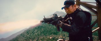 Movie still from “The Expendables 2” (2012), directed by Simon West – A man is holding a machine gun in his hand; Medium shot, Low angle