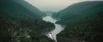 Movie still from “The Expendables 2” (2012), directed by Simon West – A boat traveling down a river surrounded by a lush green forest; Extreme Wide shot, High angle