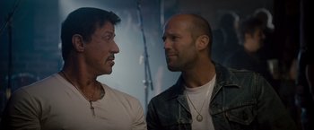 Movie still from “The Expendables 2” (2012), directed by Simon West – A couple of men standing next to each other; Close Up shot, Over the shoulder angle