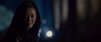 Movie still from “The Expendables 2” (2012), directed by Simon West – A woman smiles at the camera with a light shining on her face; Close Up shot, Low angle