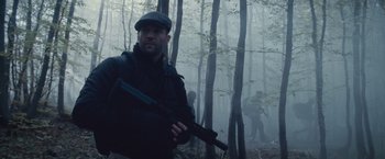 Movie still from “The Expendables 2” (2012), directed by Simon West – A man holding a rifle in a forest; Medium shot, Low angle