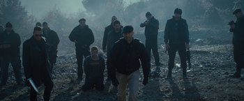 Movie still from “The Expendables 2” (2012), directed by Simon West – A group of men standing on top of a dry grass field; Wide shot, Low angle