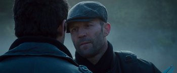 Movie still from “The Expendables 2” (2012), directed by Simon West – A man wearing a hat and a leather jacket looking at another man; Close Up shot, Over the shoulder angle