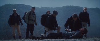 Movie still from “The Expendables 2” (2012), directed by Simon West – A group of people sitting on the ground near a hill; Wide shot, Low angle