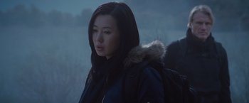 Movie still from “The Expendables 2” (2012), directed by Simon West – A young woman with a backpack is wearing a parka; Close Up shot, Over the shoulder angle