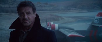 Movie still from “The Expendables 2” (2012), directed by Simon West – A man standing in front of an airplane in the dark; Close Up shot, Over the shoulder angle