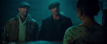 Movie still from “The Expendables 2” (2012), directed by Simon West – A man wearing a green hat and a black jacket; Medium shot, Over the shoulder angle