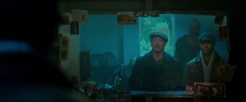 Movie still from “The Expendables 2” (2012), directed by Simon West – A man sitting at a table in front of a projection screen; Medium shot, Over the shoulder angle