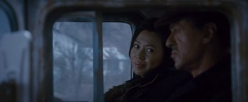 Movie still from “The Expendables 2” (2012), directed by Simon West – A woman sitting next to a man on a bus; Close Up shot, Over the shoulder angle