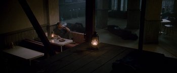 Movie still from “The Expendables 2” (2012), directed by Simon West – A man sitting at a table in a restaurant smoking a cigarette; Wide shot, High angle