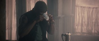 Movie still from “The Expendables 2” (2012), directed by Simon West – A man drinking a cup of coffee from a mug; Medium shot, High angle