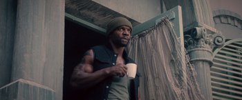 Movie still from “The Expendables 2” (2012), directed by Simon West – A man holding a coffee cup while standing next to a window; Medium shot, Low angle