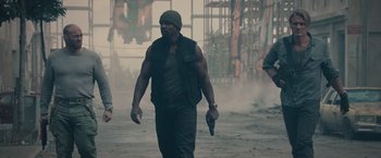 Movie still from “The Expendables 2” (2012), directed by Simon West – A man walking down a street holding a gun; Medium shot, Low angle