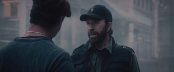 Movie still from “The Expendables 2” (2012), directed by Simon West – A man wearing a baseball cap talking to another man; Close Up shot, Over the shoulder angle