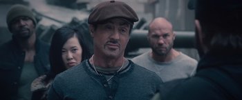 Movie still from “The Expendables 2” (2012), directed by Simon West – A man in a brown hat standing in front of two other men; Close Up shot, Over the shoulder angle