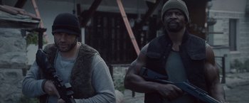 Movie still from “The Expendables 2” (2012), directed by Simon West – Two men are standing together holding guns; Medium shot, Over the shoulder angle