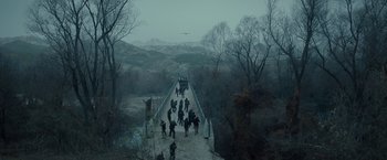 Movie still from “The Expendables 2” (2012), directed by Simon West – A group of people walking across a snow covered bridge; Extreme Wide shot, High angle